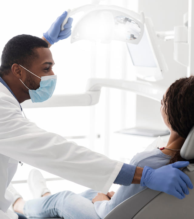 Side view of young African American stomatologist talking to his female patient sitting in dentist chair