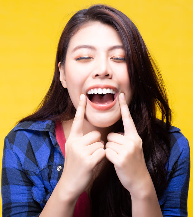 Beautiful asian woman smiling widely at the camera and pointing to her healthy gums