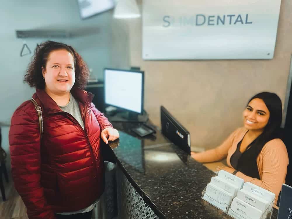 Slim Dental reception desk with receptionist and patient smiling